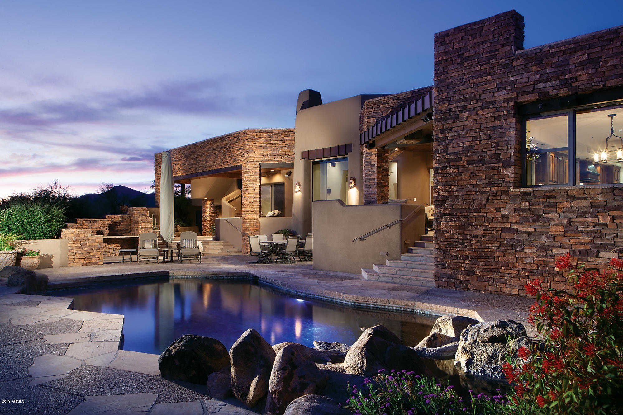 Luxury desert home, Southwestern architecture, stone exterior, custom home, swimming pool, outdoor living, twilight photography, Arizona real estate, mountain views (implied distant), high-end residential, custom home builder, resort-style living, dream home, architectural lighting, outdoor entertainment.