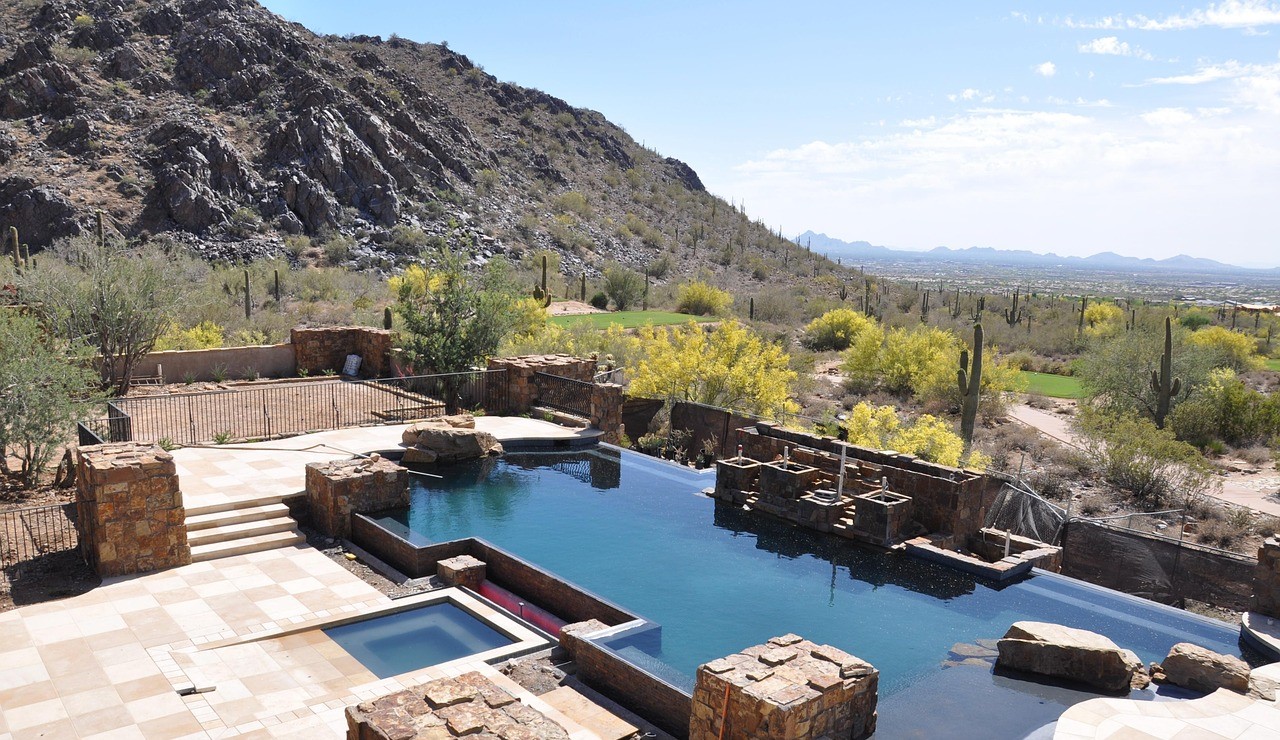 Luxury custom pool, infinity edge pool, mountain view, desert landscape, Arizona pool, resort-style backyard, stone water features, spa pool, paver patio, custom home amenities, high-end pool design, desert oasis, outdoor living space, residential pool, large property.